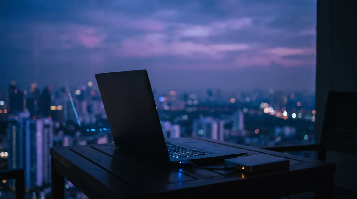 A laptop and portable drive on a hotel balcony at blue hour above city lights