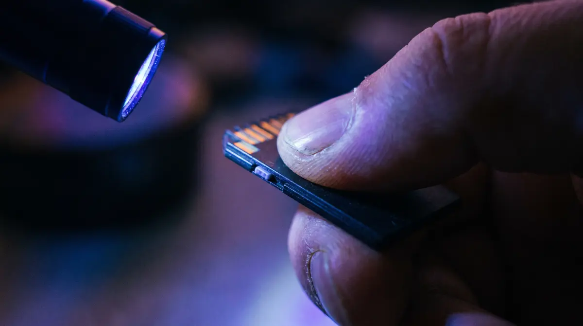 A fingertip slides the tiny lock switch on a memory card under a penlight beam