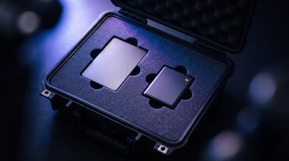 An open equipment case with foam cutouts holding a portable drive and a card reader