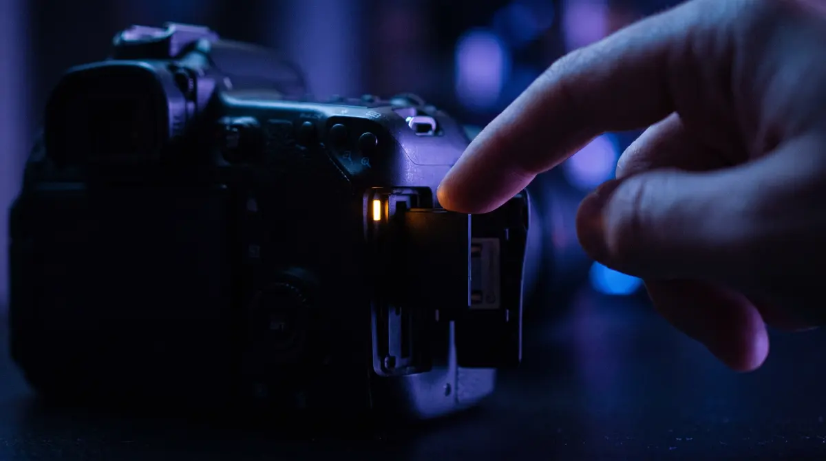 A hand waits at a camera's card slot while a small amber lamp still glows