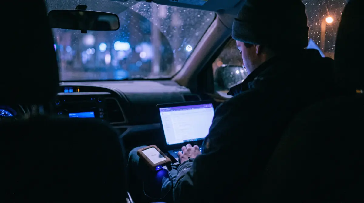 A shooter in a parked car at night checks a laptop and drive before leaving