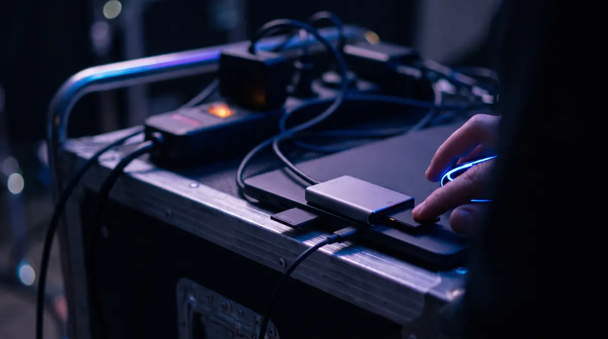 Fingers push a memory card into a laptop-connected reader on a rolling location cart