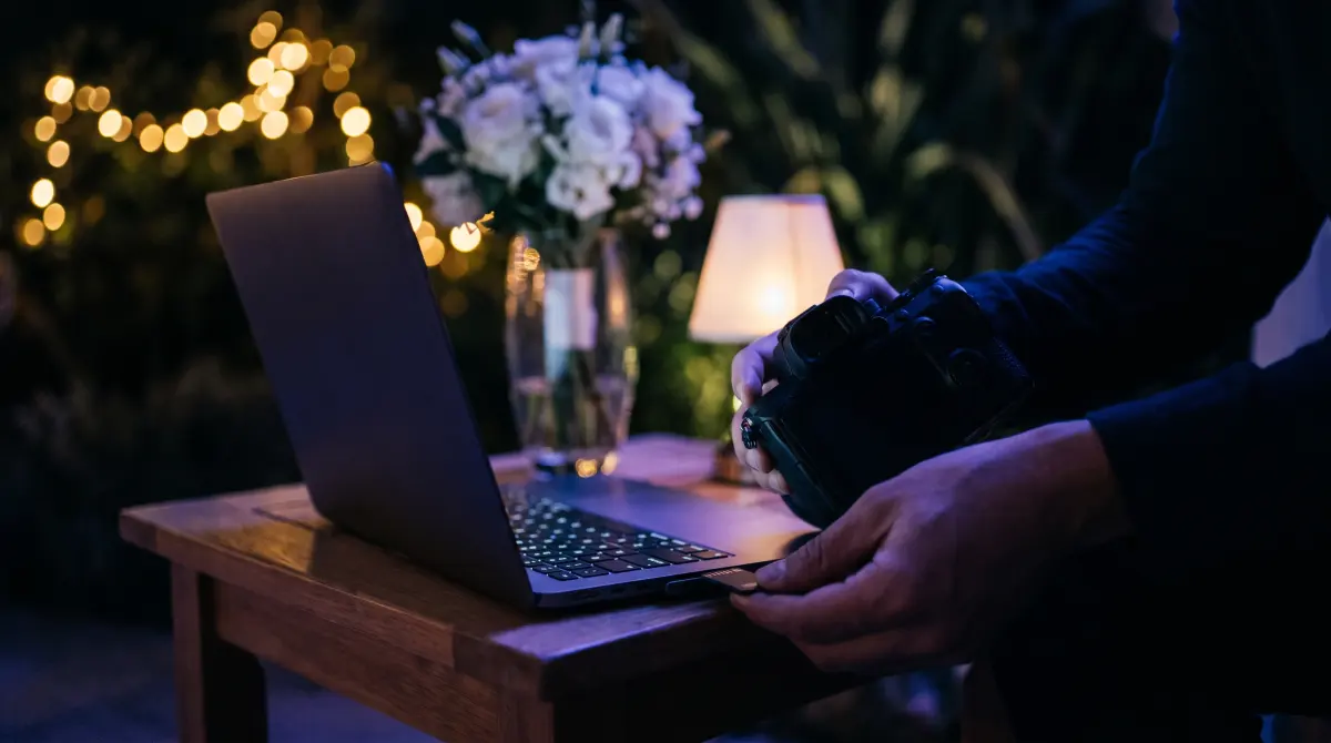 A videographer moves a camera card into a laptop reader at a night wedding